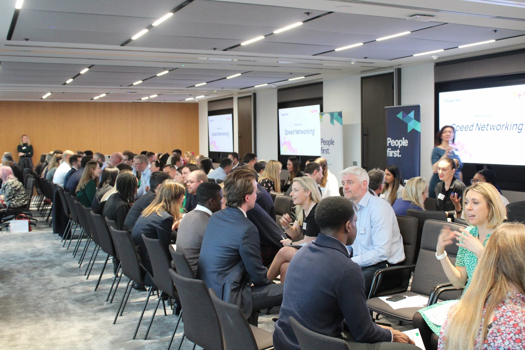 Speed networking in progress. Rows of pairs of people in chairs, talking.