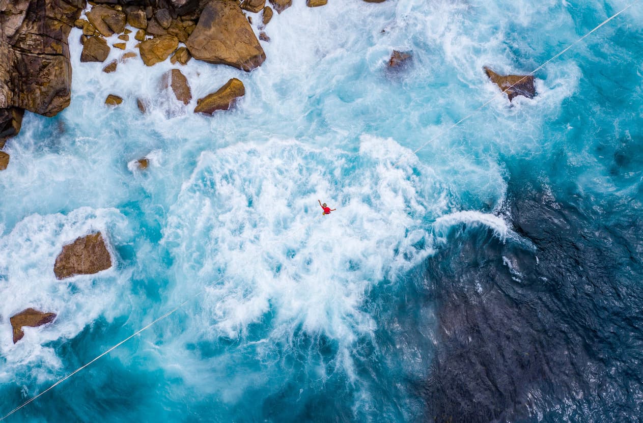 man balancing on high wire over white water rapids