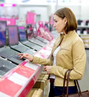 A lady in a tan leather jacket tries out a new laptop in a technology store