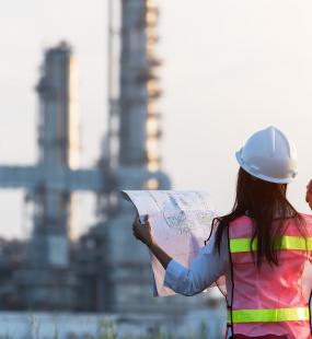 A female engineer holds up blueprints as she surveys a power station from a distance