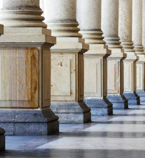 A row of marble columns with the sunlight shining through, casting shadows on the floor