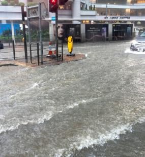 A woman tries to cross a heavily flooded high street as a car drives past in deep water