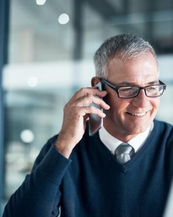A smiling business man talks on the phone in an open plan office