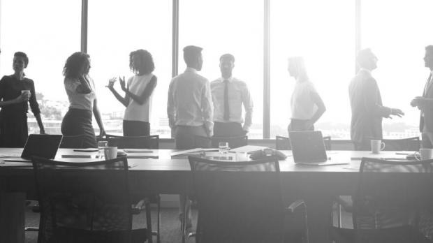 A board meeting with lots of people stood around a table