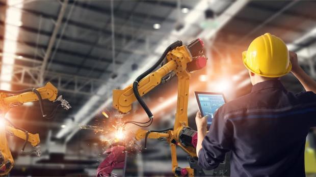 An engineer using a tablet computer checks the progress of automated robotic welding arms in a factory