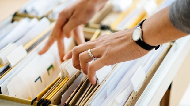 Hands move files in a filing cabinet