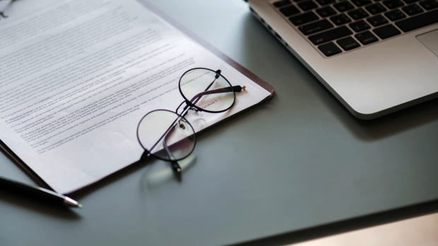A pair of glasses resting on a contract next to an open laptop
