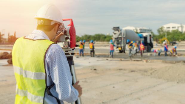 A surveyor on a building site looks through a theodolite