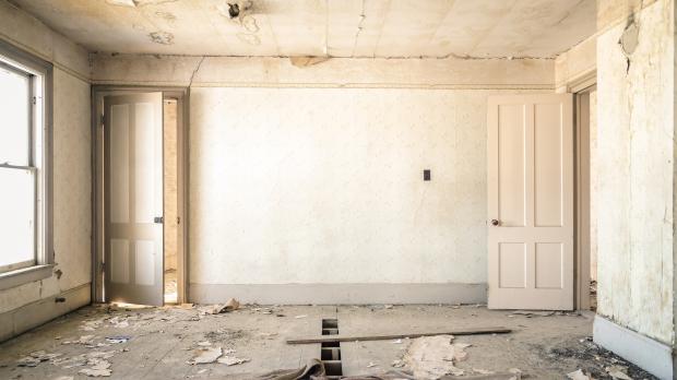 An empty room mid-renovation, with plaster falling off the wall and the floor torn up