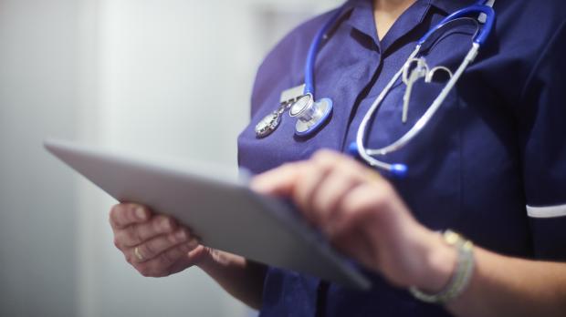 A nurse in blue scrubs using an ipad