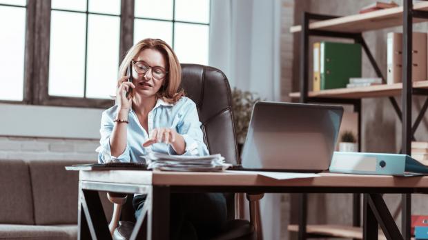 Female solicitor sitting at desk on mobile phone in front of laptop